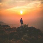 A lone hiker admires a stunning sunset view from Ponmudi Peak, creating a serene landscape scene.